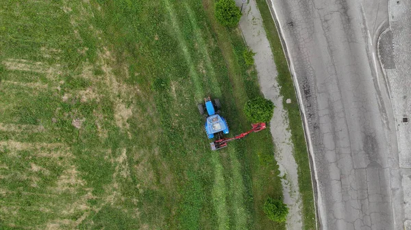 Yol boyunca traktör ve çim biçme makinesiyle çim biçen bir çiftçinin hava görüntüsü, iyi korunmuş ve resimli kırsal bir manzaraya katkıda bulunuyor.