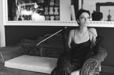 Sofistike zarafet ve klasik cazibe tasvir eden bir kadın lüks bir koltuğa oturmuş elinde sigara tutacağı ve güneş gözlüğü tutarak klasik moda ve yaşam tarzını yansıtıyor.