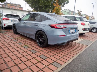 Siyah alaşımlı tekerleri olan modern bir Honda Civic hatchback dışarıda, desenli tuğladan bir kaldırımda park halinde.