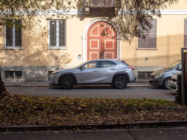 Günümüz gümüş rengi Lexus UX kavşağı, sonbaharda bir caddede, kaldırımı kaplayan yapraklarla ve arka planda eski bir binayla park edilmiştir.