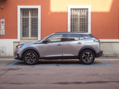 Günümüz gümüş rengi bir Peugeot 2008 SUV 'si, kentsel bir caddede belirlenmiş bir yere park edilmiş, desenli turuncu bir duvara karşı parlak tasarımını sergiliyor.