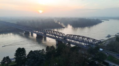Güneş, İtalya 'nın Cremona kenti yakınlarındaki Po Nehri' ni kaplayan büyük bir demiryolu köprüsüne yumuşak bir parıltı saçarak sisli bir arazide yükselir.