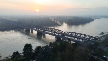 Güneş, Po Nehri 'nin üzerine ılık bir parıltı ve Lombardiya' daki tarihi bir demiryolu köprüsünden doğar.