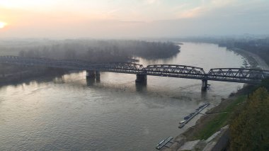 Muhteşem bir çelik kiriş köprüsü Po Nehri boyunca uzanır, sabah sisi içinde, güneş doğarken Lombardy manzarası üzerinde