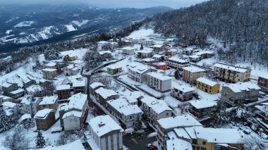 Hava perspektifi, taze karla kaplanmış, çatılarını ve Le Bore, PR, İtalya çevresindeki orman yamaçlarını gözler önüne seren tuhaf bir İtalyan dağ köyünü yakalıyor.