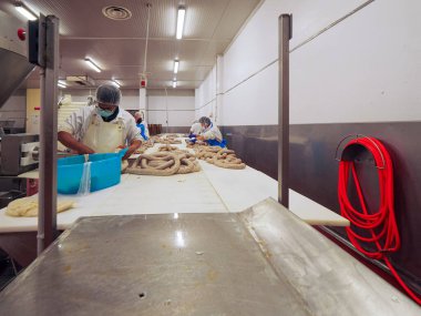 Temiz, steril gıda işleme fabrikasındaki çalışanlar aktif olarak sosis yapma sürecine girerek hijyen ve kalite kontrolü sağlıyorlar.