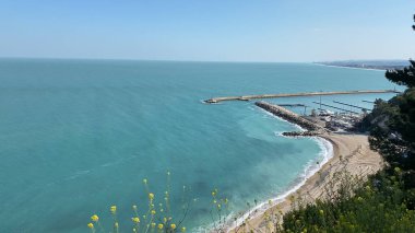 Numana, İtalya - 22 Nisan 2023 Bu çarpıcı kıyı manzarası ile huzur içinde kayalık bir kıyı şeridi, canlı sarı çiçekler ve sakin bir okyanus manzarası. Seyahat, doğa ve...