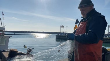 Numana, İtalya - 22 Nisan 2023 Bir balıkçı sakin deniz kıyısında sakin mavi bir gökyüzünün altında balık ağını hazırlıyor. Sahne, bir huzur ve sükunet hissi yayıyor.