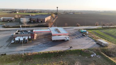 Piacenza 'daki SS 10 Strada Statale Padana Inferiore benzin istasyonunda. İtalya. Kamyon yakıtlı. Endüstriyel binalar ve tarım alanlarıyla çevrili engin bir gökyüzünün altında