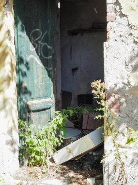 Yabani otlarla kaplanmış ve enkazla kirlenmiş terk edilmiş bir kapı manzarası ihmal ve çürüme hissi uyandırıyor..