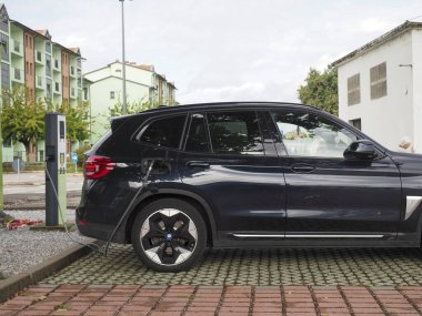 Crema, İtalya - 5 Temmuz 2025 Çağdaş bir şehirde çevre dostu ulaşım sergilenen modern bir şehir istasyonunda parlak siyah elektrikli bir SUV şarj ediliyor.