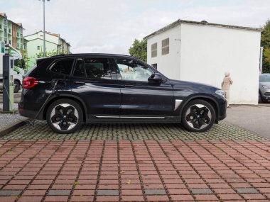 Crema, İtalya - 5 Temmuz 2025 Şık siyah bir BMW SUV, modern bir şehir ortamında çevre dostu ulaşım sergiliyor. Parlak araç tuğlalı bir kaldırıma park edilmiş.