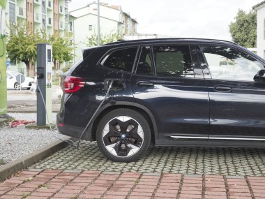 Crema, İtalya - 5 Temmuz 2025 Modern bir şehir şarj istasyonunda siyah bir BMW elektrikli SUV, çevre dostu ulaşım ve daha temiz bir gelecek için sürdürülebilir enerji çözümleri sergiliyor.