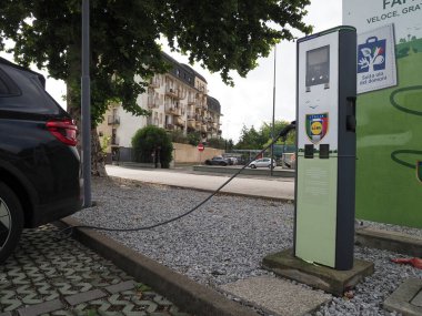 Crema, İtalya - 5 Temmuz 2025 Modern kentsel şarj istasyonunda elektrik yüklü yeşil ışıklı, sürdürülebilir şehir yaşamı ve daha temiz bir şehir için çevre dostu ulaşım çözümleri sunan