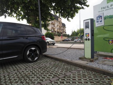 Crema, İtalya - 5 Temmuz 2025 Modern bir şehir şarj istasyonunda siyah elektrikli araba, yeşil girişimleri ve sürdürülebilir yaşam koşulları olan bir şehirde çevre dostu ulaşım sergiliyor.