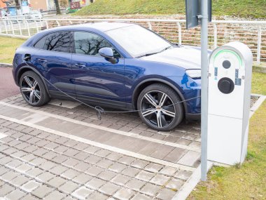 Cremona, İtalya 9 Ocak 2026 Mavi Porsche Cayenne E Hybrid SUV bataryasını EV istasyonunda şarj ediyor, elektrohareketlilik, sürdürülebilirlik ve melez teknolojisi sergiliyor