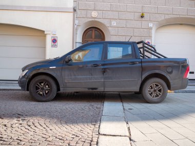 Cremona, İtalya 9 Ocak 2026 SsangYong Musso Musso siyah kamyonet eski bir kaldırım taşı caddesinde konut binalarının önünde, yan görüş