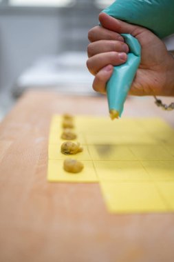 Şefin el borusu ahşap bir tahta üzerinde kare sarı tortelli üzerine doluyor, profesyonel bir mutfakta yeni yapılmış doldurulmuş makarnayı kapatıyorlar otantik İtalyan mutfağını hazırlıyorlar.
