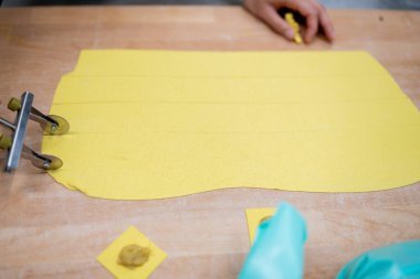 Taze tortelli makarna hazırlayan, hamur işini makarna tekerleğiyle kesen ve küçük meydanları geleneksel dolduran ellerin yakın plan görüntüsü.