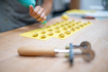 Şefin elleri taze tortelli makarna hazırlıyor. Profesyonel bir Toskana mutfağındaki ahşap tezgahın üzerine geleneksel dolgu malzemelerini yerleştiriyor. Orijinal İtalyan mutfağını garantiliyor.