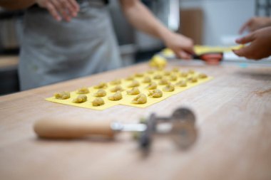 Profesyonel aşçılar ahşap tezgahın üzerinde el yapımı tortelli şekillendirerek otantik İtalyan mutfağı için işlek bir ticari mutfakta taze makarna doldurup mühürlüyorlar.