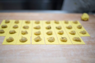Sıralar dolusu taze makarna kareleri doldurulmuş, lezzetli tortelli şeklinde katlanmaya hazır, otantik İtalyan mutfak sanatları sergileniyor.