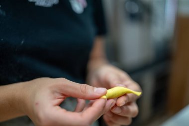 Yakın plan çekimde, İtalyan makarna yapma sürecini vurgulayan bir tortelli 'yi titizlikle hazırlayan kişinin elleri görülüyor.