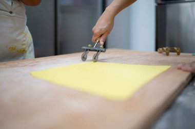 Profesyonel bir aşçı geleneksel İtalyan tortelli taze makarna hazırlıyor, profesyonel bir mutfakta hamur işi makarnayla makarna kesiyor ve Toskana yerel yemek kültürünü sunuyor.