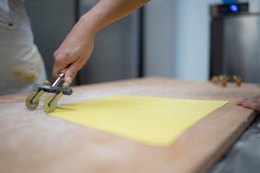 Yakın plan çekimde, tortelli 'ye hazırlanmak için hamur işi kesmek için hamur işi kullanan bir kadın elleri görülüyor.