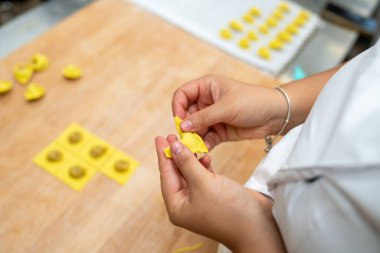 Bir insanın el yapımı tortelli hamur hamurunu ahşap bir yüzeye titizlikle katlayıp mühürlediği yakın çekim görüntüsü aşçılık yeteneği ve taze malzemeler sergiliyor.
