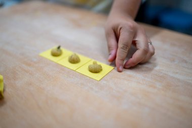 Bir kadının ellerinin ahşap bir yüzeyde küçük, doldurulmuş makarna karelerini dikkatlice şekillendirerek klasik bir İtalyan yemeği hazırlarken yakın plan çekimi.