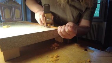 Yetenekli bir zanaatkar, özel bir uçak ve el aletleri ile bir atölye ayarında ahşap bir yay çubuğunu titizlikle şekillendirir.