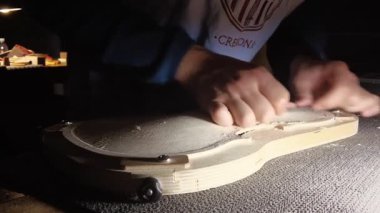 Cremona, İtalya - 18 Şubat 2022 Bir zanaatkarın elleri dikkatle oyma ve kum Bir keman bitmemiş ahşap gövde, araçlar ve talaş ile çevrili tarihi bir İtalyan lutherie
