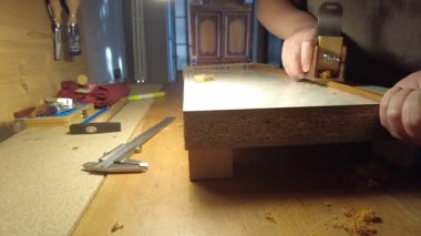 Aletler ve talaşlarla çevrili bir odun parçası üzerinde dikkatlice çalışan bir Luthier 'in ellerinin yakın plan görüntüsü.