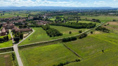 Procaccini Şatosu mimarisi görkemli bir şekilde yemyeşil tarım tarlalarının ve İtalya 'nın Pavia kentindeki Chignolo Po köyünün ortasında duruyor. Uçsuz bucaksız mavi gökyüzünün altında beyaz bulutlar var.