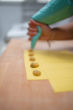 Şef ev yapımı ravioli için taze makarna hamuru kareleri dolduruyor.