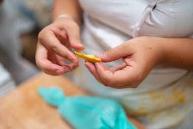 Ev yapımı makarna ya da hamur tatlısı için sarı hamuru şekillendiren ellerin yakın çekimi