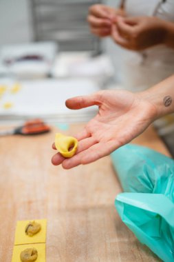 Yeni yapılmış bir tortellini makarnasını tutan ve İtalyan yemeği hazırlayan bir elin yakın çekimi.