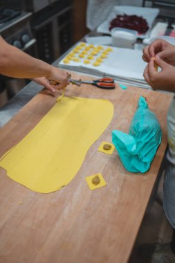 Eller taze makarna hamuru yapıyor ve ahşap bir tahtaya ravioli dolduruyor.