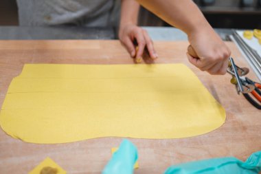 Şef taze makarna hamurunu ahşap bir tahtanın üzerinde hamur tekeriyle şeritler halinde keser.