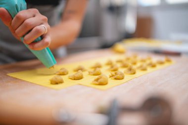 Şef dikkatli bir şekilde ev yapımı ravioli için taze makarna hamuru kareleri dolduruyor.
