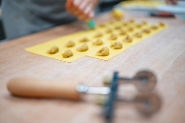 Ev yapımı ravioli, yakınlarda hamur işi tekerleği olan sarı bir makarna tepsisinde dikkatlice hazırlanıyor.