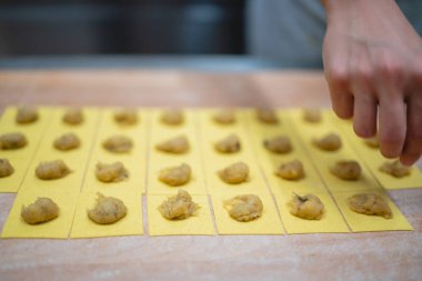 Şefin elleri dikkatlice ravioli yapmak için taze makarna karelerine dolduruyor.