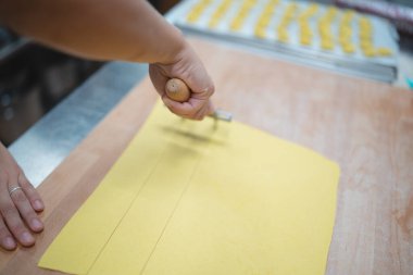 Ev yapımı makarna hamuru ahşap bir tahtanın üzerinde hamur tekeriyle dilimleniyor.