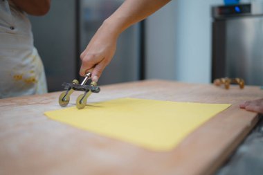 Fırıncının elleri, ahşap bir masada iki tekerlekli pasta kesiciyle taze makarna hamurunu tam olarak kesti.