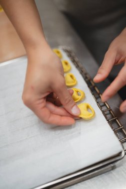 Elleri dikkatle yeni yapılmış tortellini makarnasını parşömen kağıdıyla kaplı bir çarşafa yerleştiriyor.
