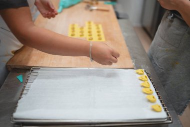 Eller dikkatlice, yeni yapılmış tortellini 'yi mutfak ortamındaki soğutma rafına yerleştiriyor.