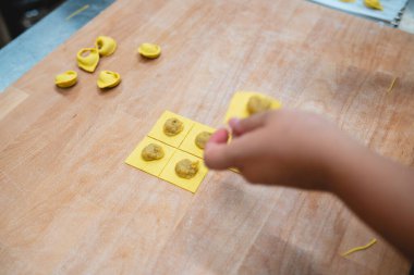 Çocuğun elleri tahta kesme tahtasıyla doldurulmuş taze tortellini makarna yapıyor.