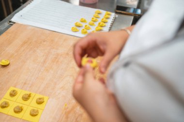 Aşçı elleri dikkatle ahşap kesme tahtasının üzerinde taze tortellini makarna yapıyor.
