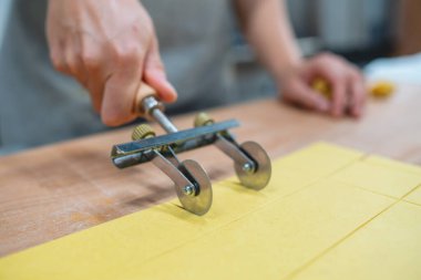 Makarna keskisi kullanarak ahşap bir tahtanın üzerinde taze ev yapımı hamur dilimlemek için ellerinizi yakın plan çekin.